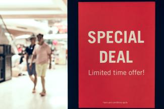 adults walking by a sign advertising a special deal