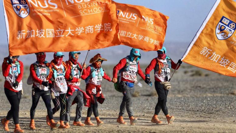NUS business school students in the Gobi desert holding flags with the NUS logo